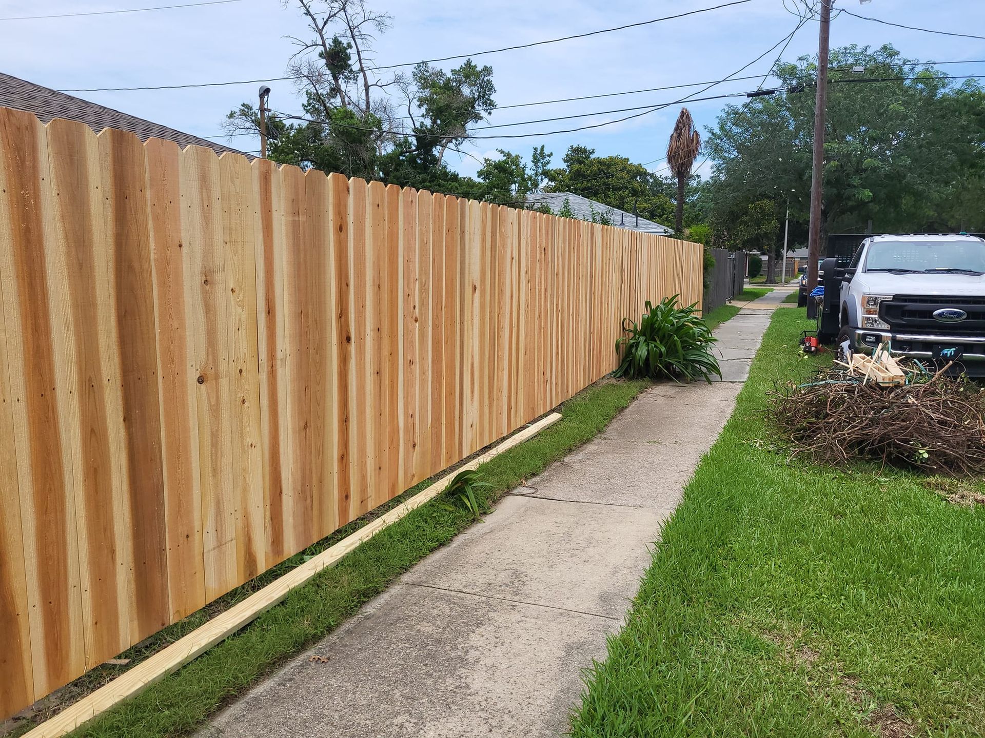 A wooden fence is being built next to a sidewalk.