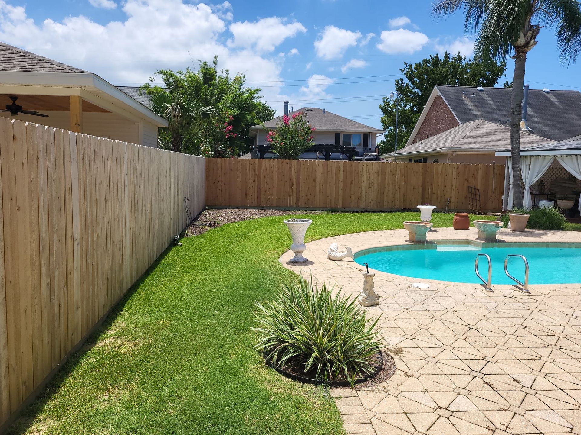 A wooden fence surrounds a swimming pool in a backyard.