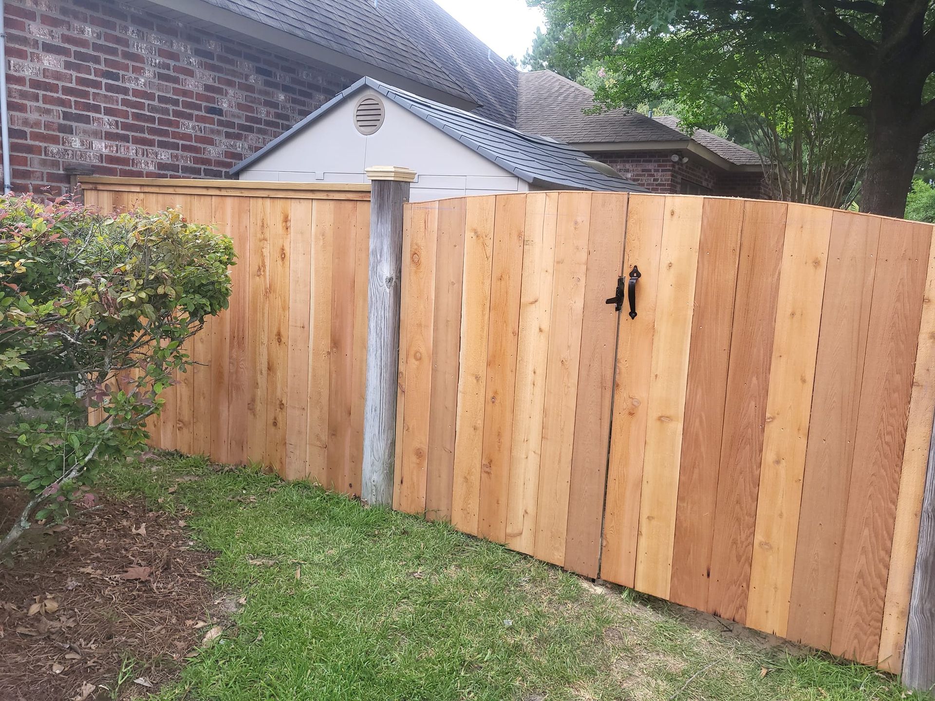 A wooden fence with a gate in front of a brick house.