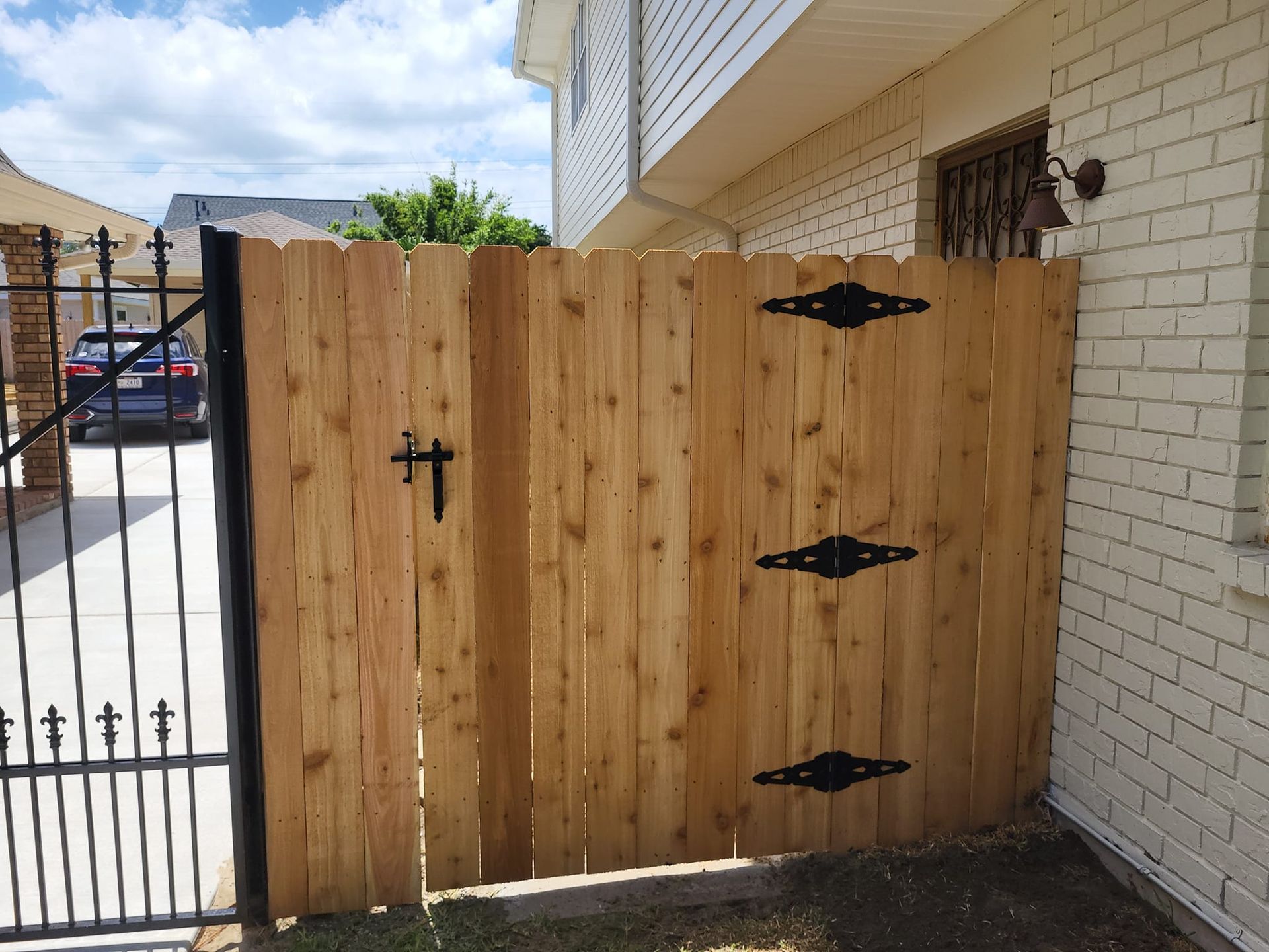 A wooden fence with a metal gate in front of a white brick building.