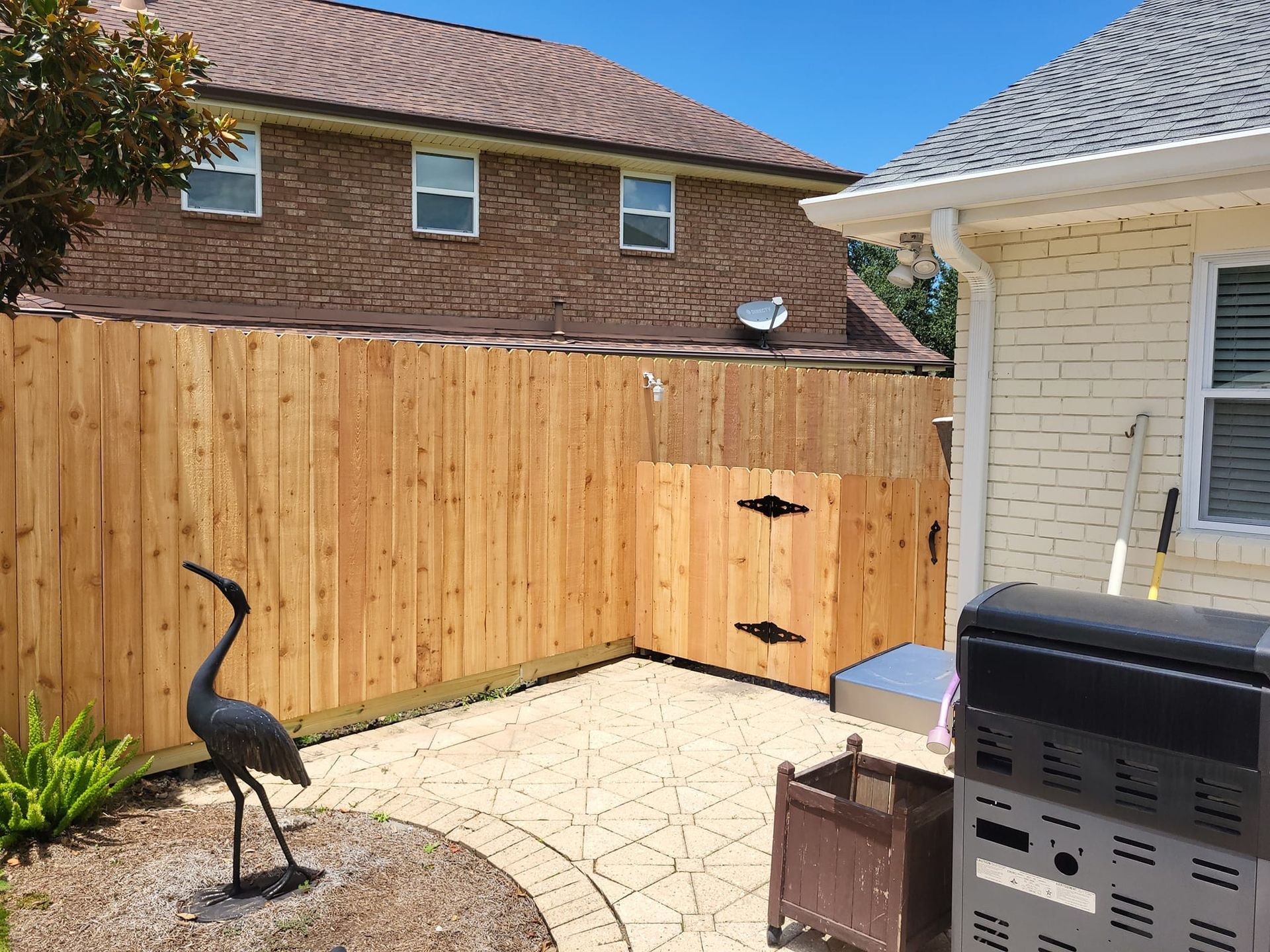 A wooden fence is in the backyard of a house with a bird statue in front of it.