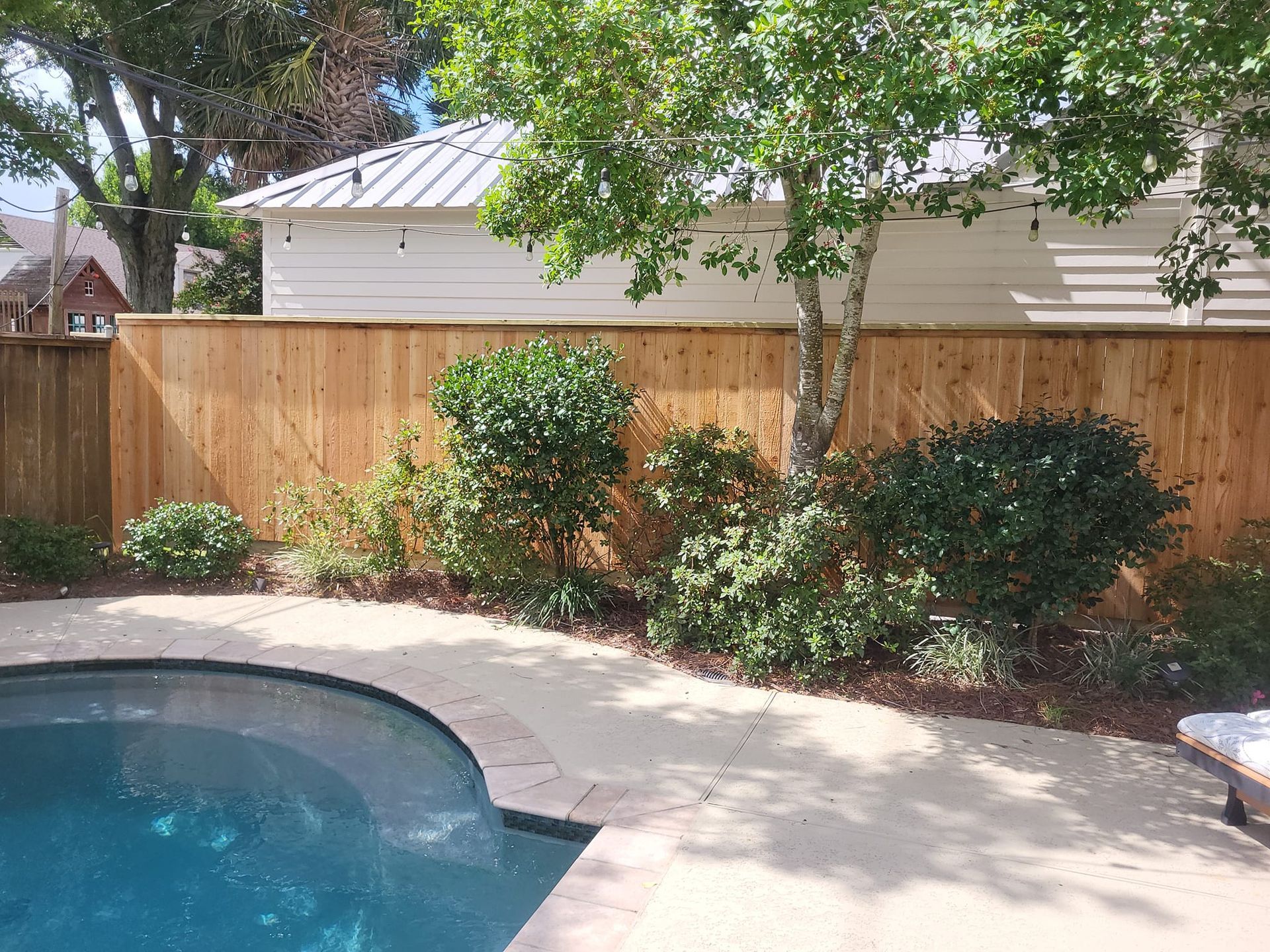 A wooden fence surrounds a swimming pool in a backyard.