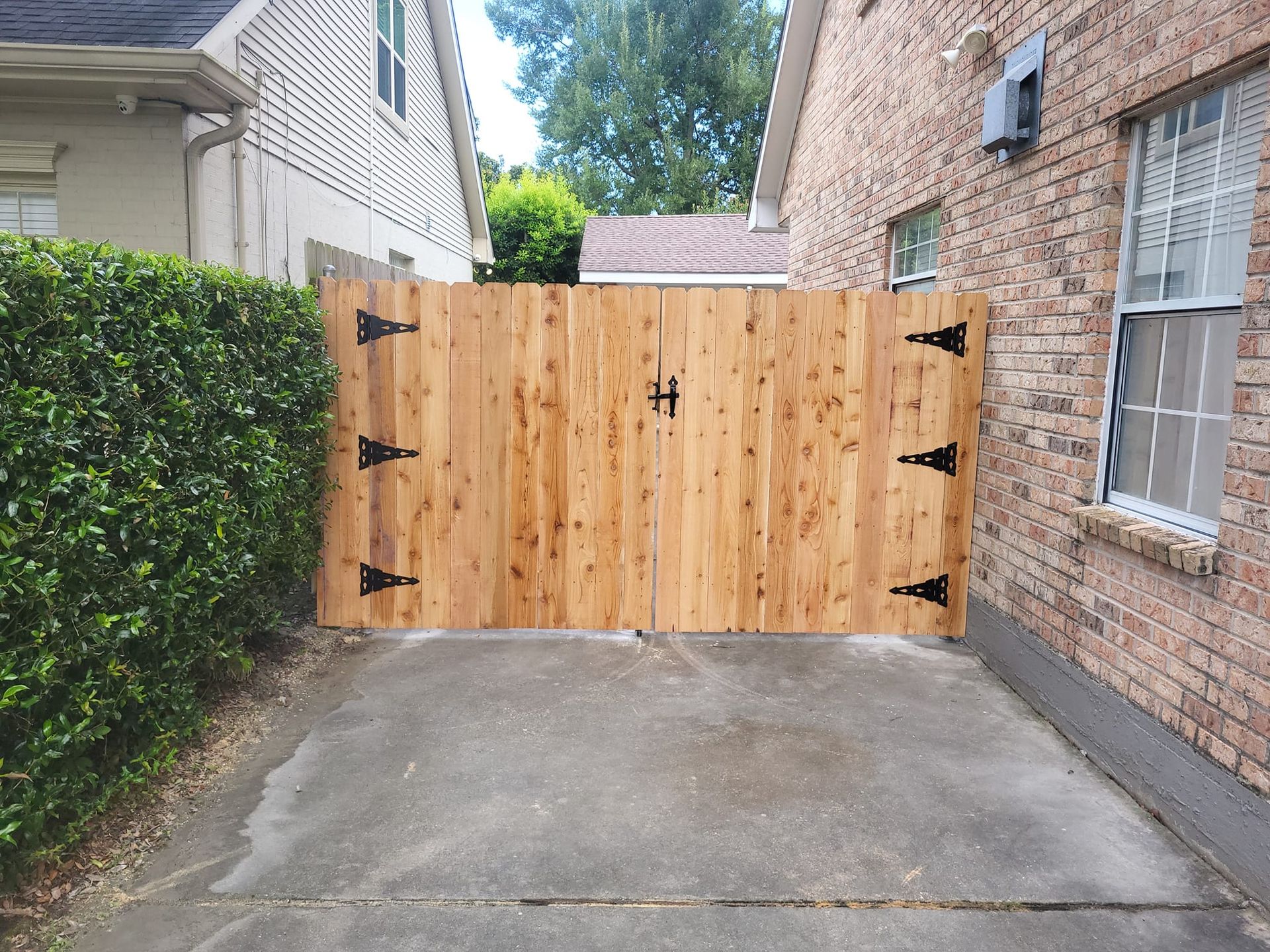 A wooden gate is in the driveway of a brick house.