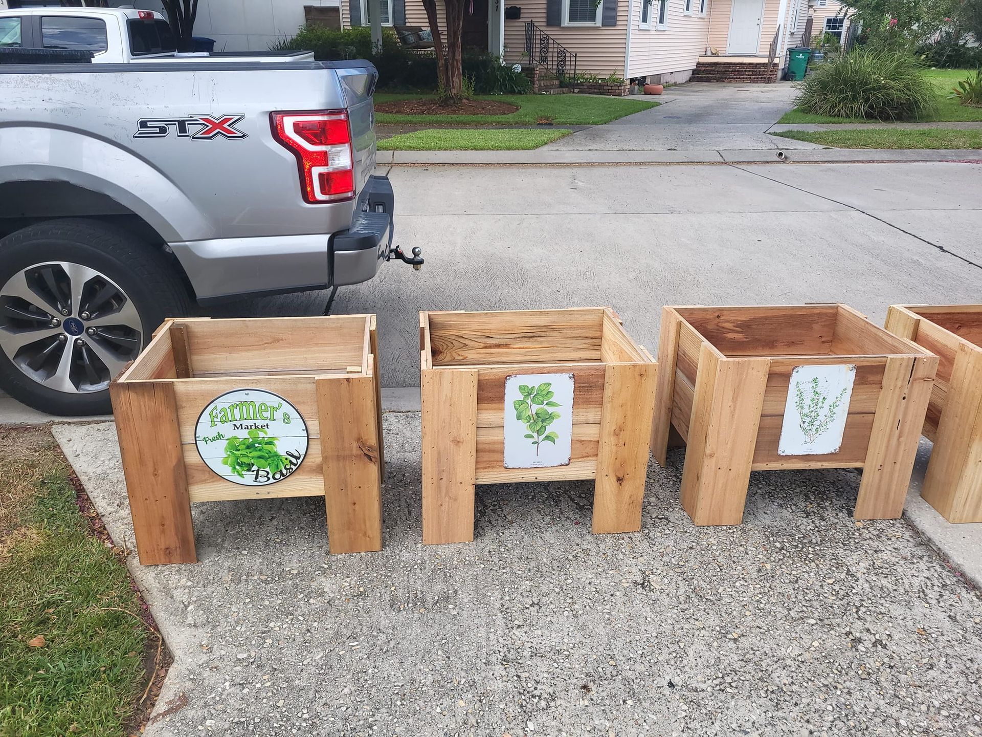 Three wooden planters are lined up in front of a silver truck.