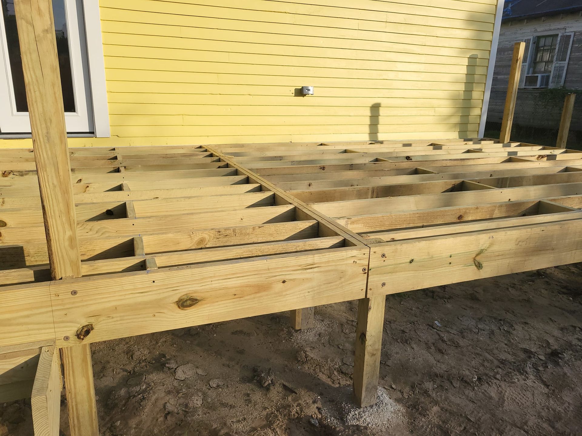 A wooden deck is being built in front of a yellow house.