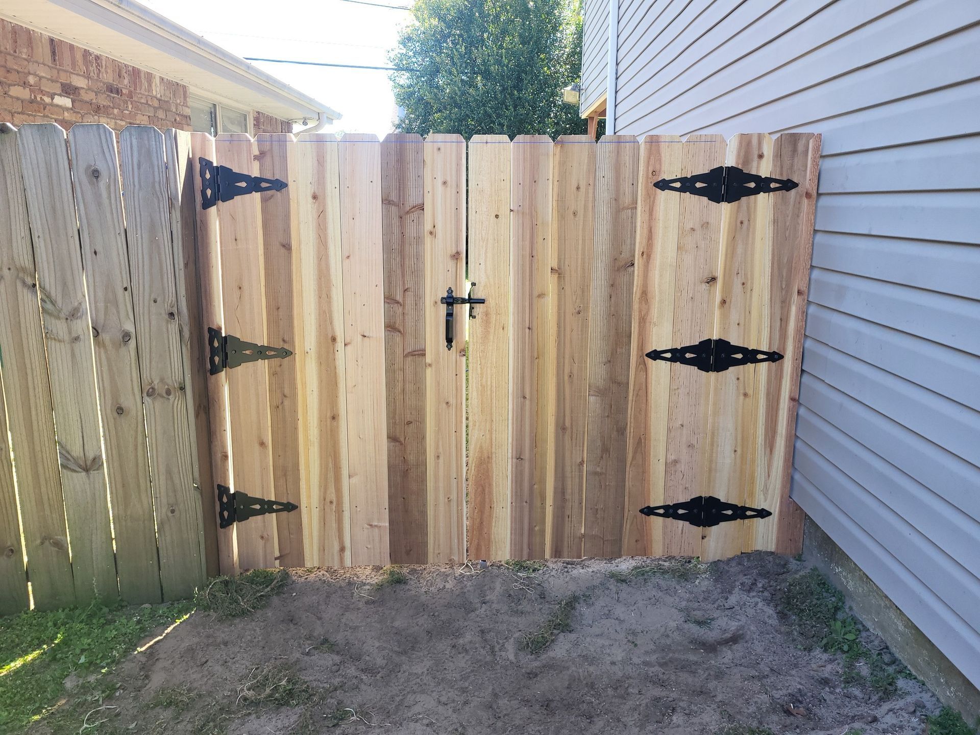 A wooden fence with black hinges is next to a house.