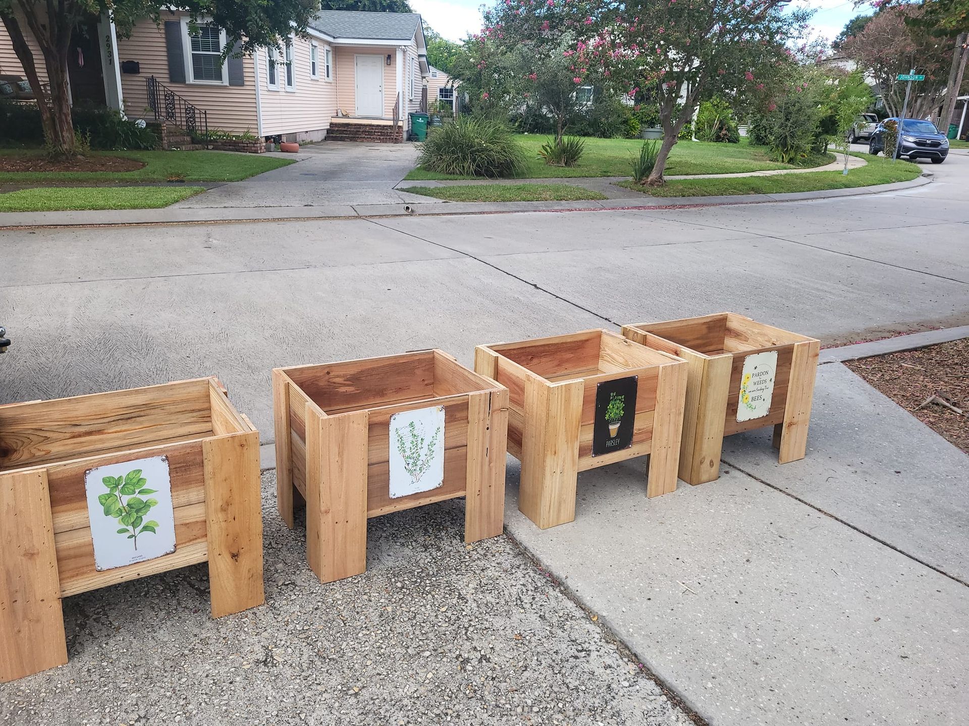 A row of wooden planters are lined up on a sidewalk in front of a house.
