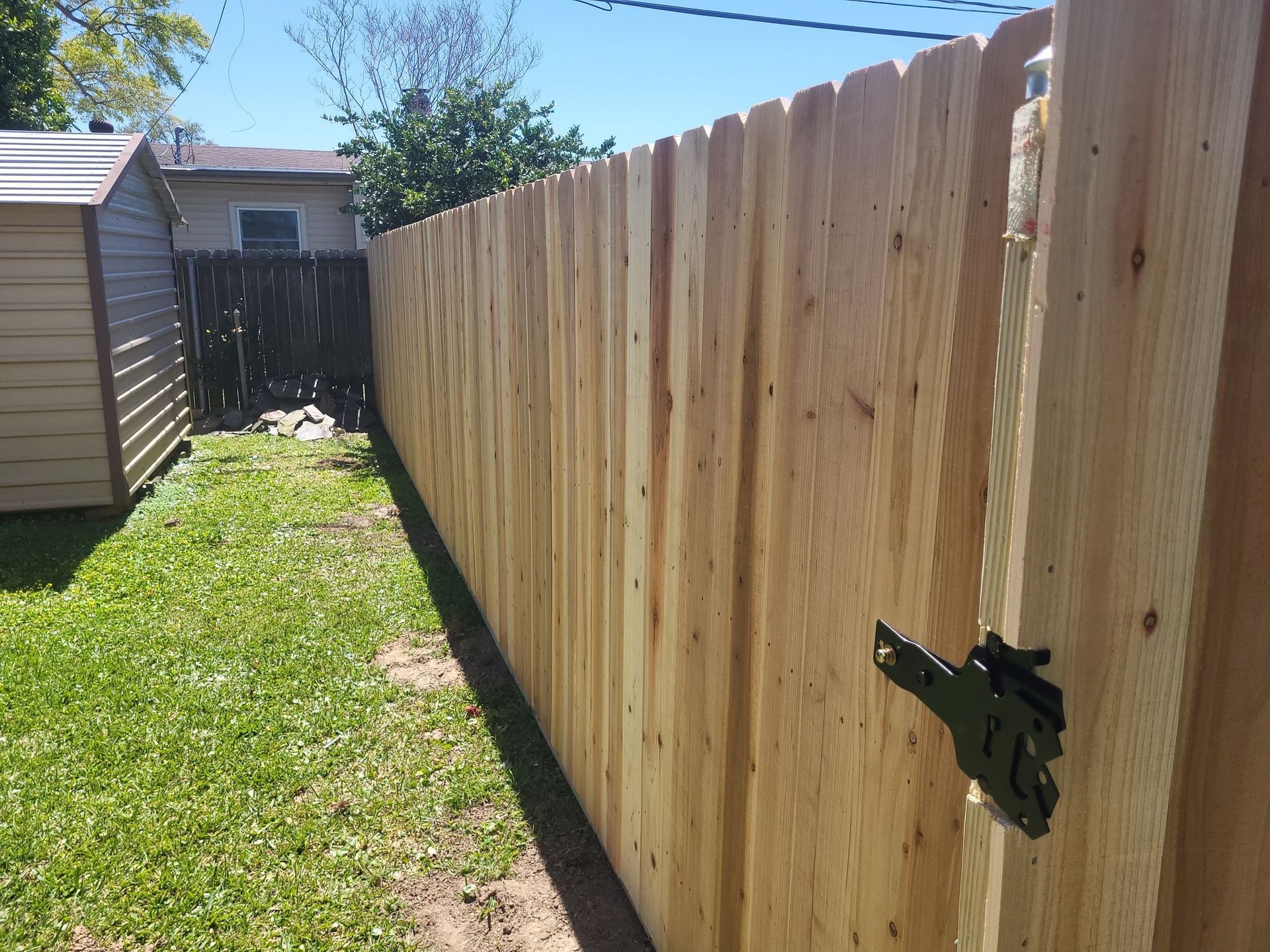 A wooden fence in a backyard with a shed in the background.