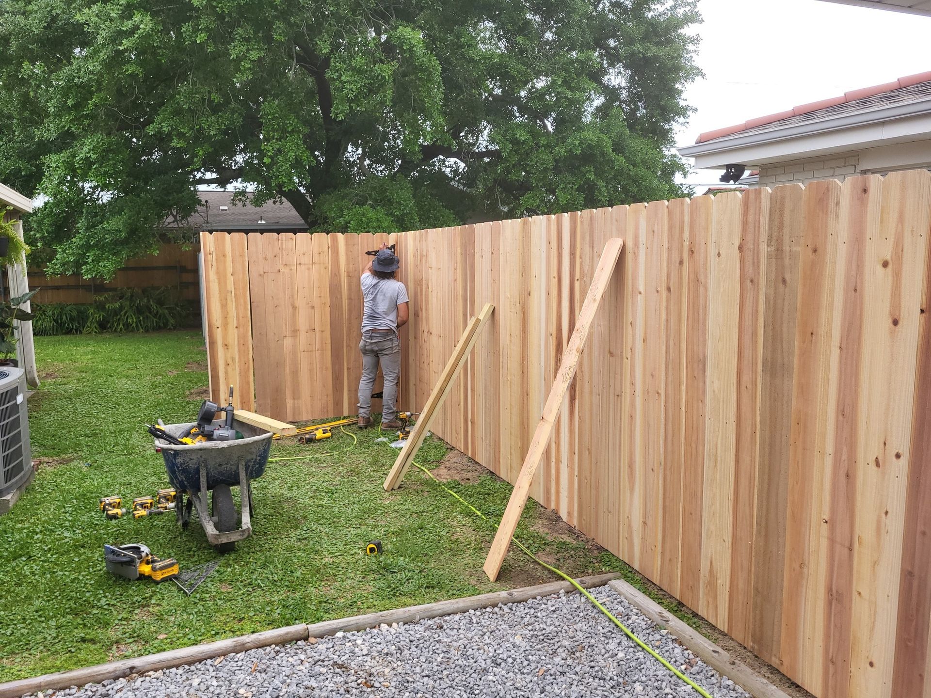 A man is standing next to a wooden fence in a backyard.