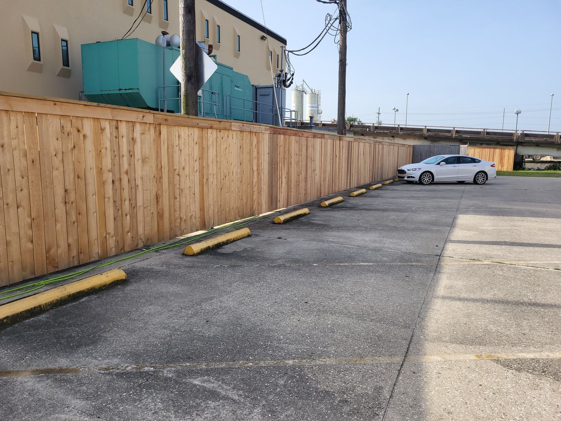 Parking lot with wooden fence, yellow wheel stops, and a white car.