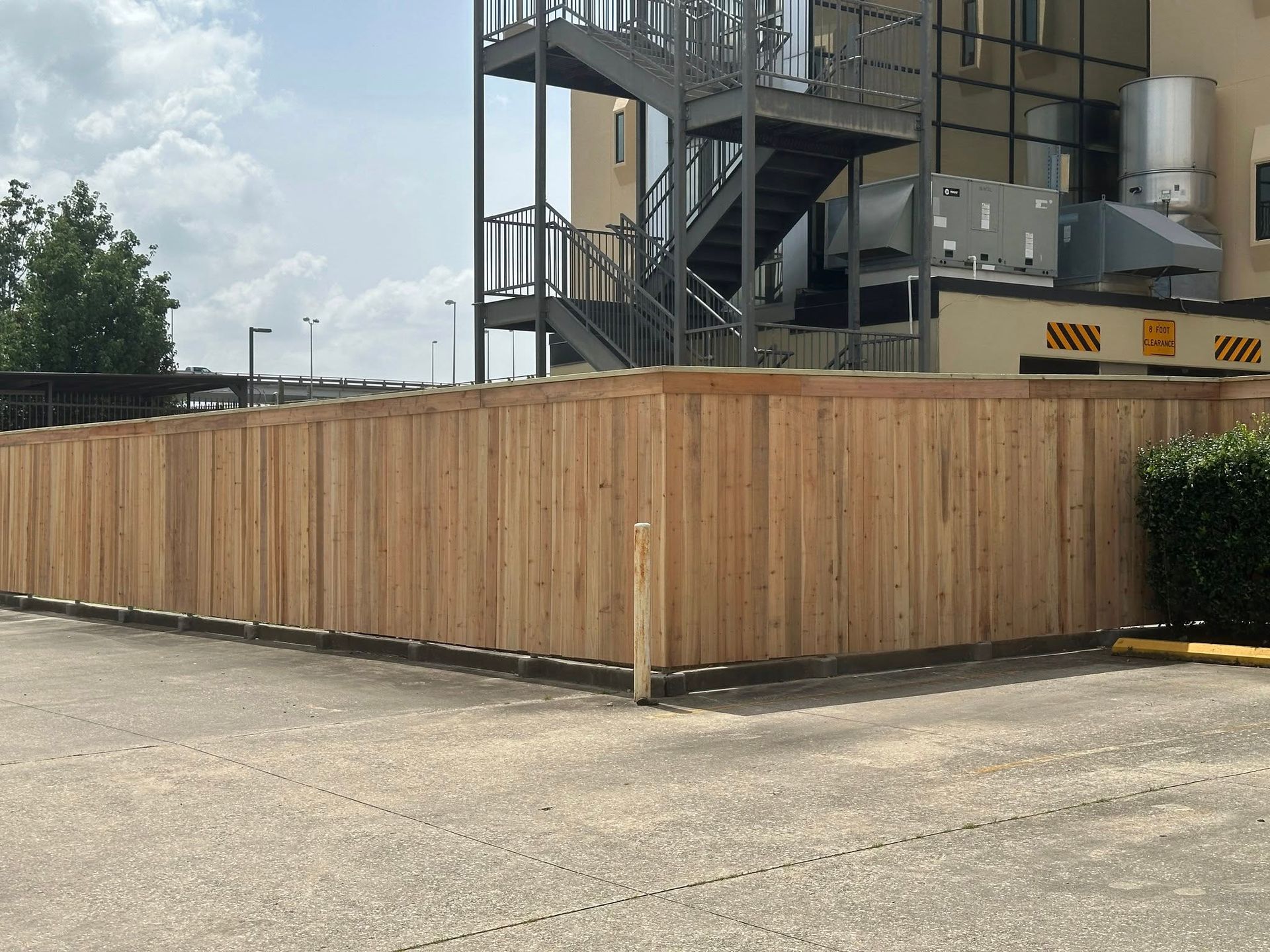 Wooden fence around an outdoor space, with an apartment building and staircase in the background.