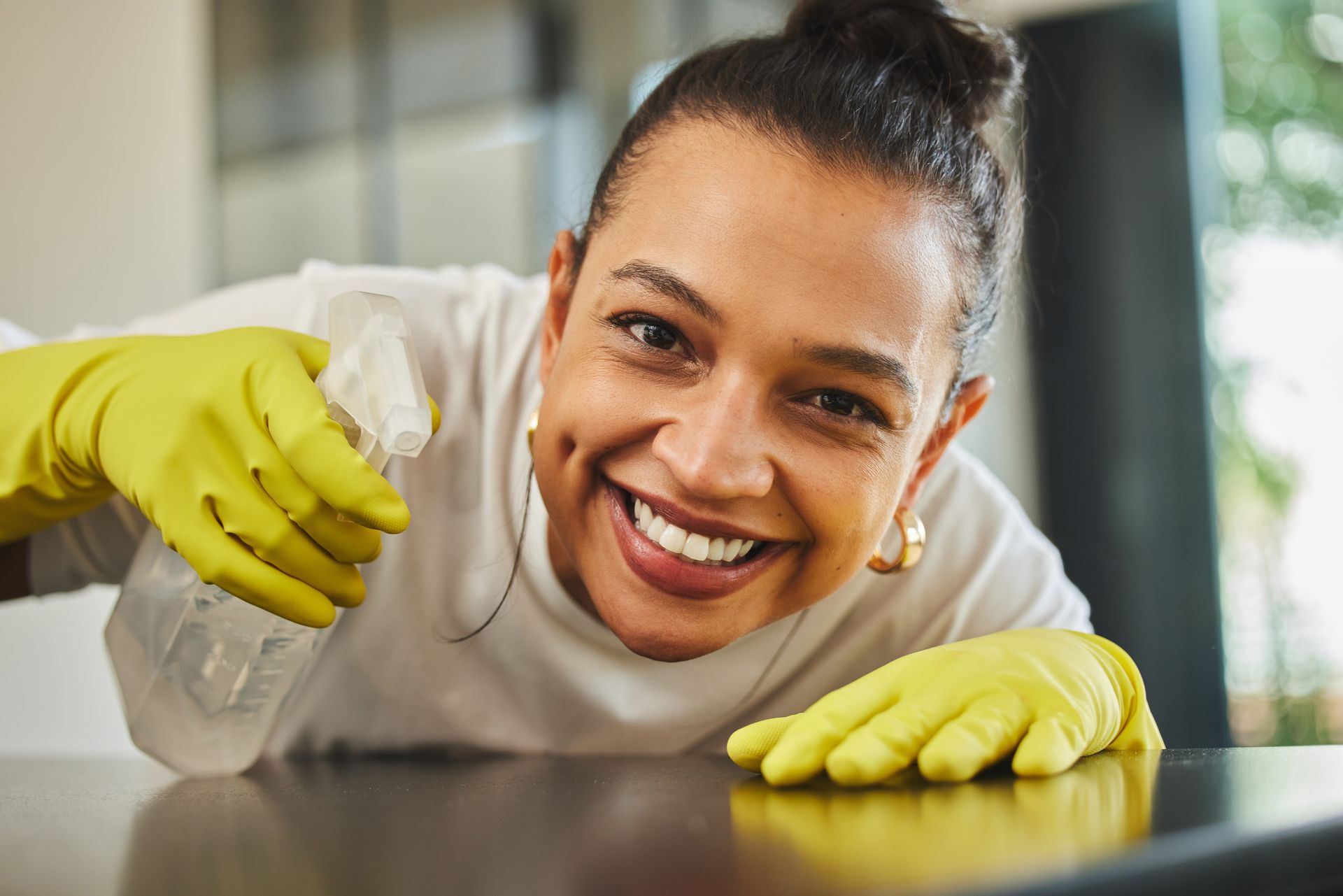 A woman wearing yellow gloves is smiling while cleaning a table.