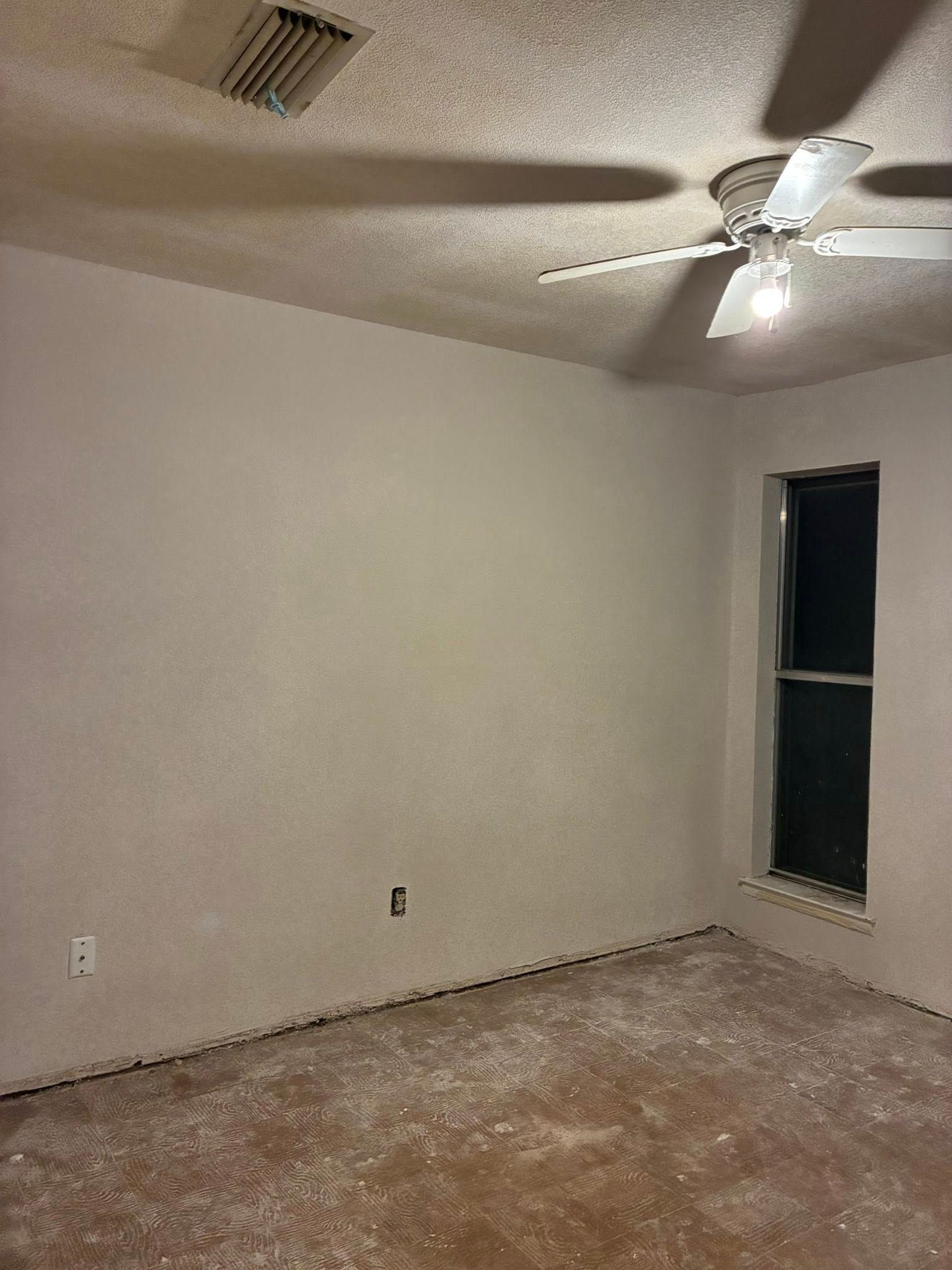 Empty beige bedroom with carpet, ceiling fan, and one small window.