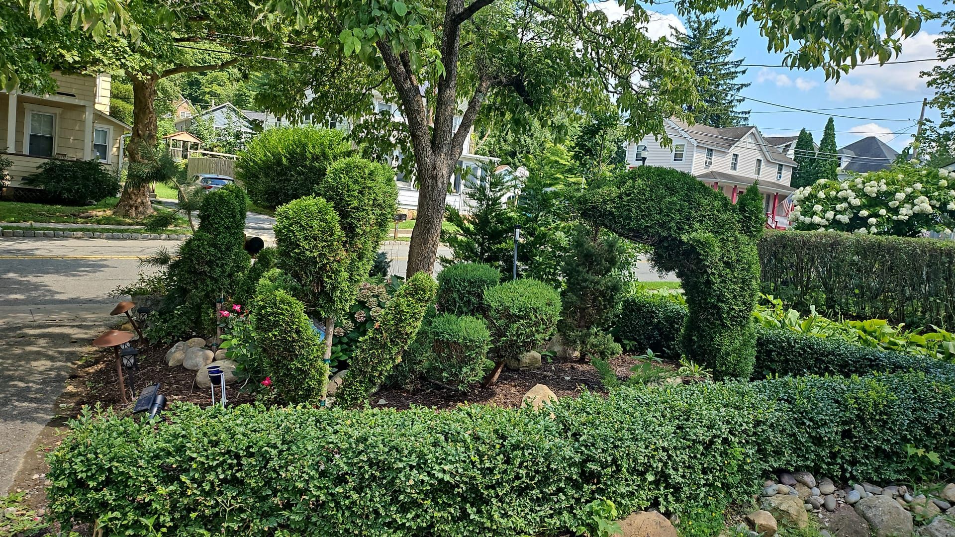 A garden with topiary plants shaped into arches and rounded forms, featuring a trimmed hedge in the foreground.