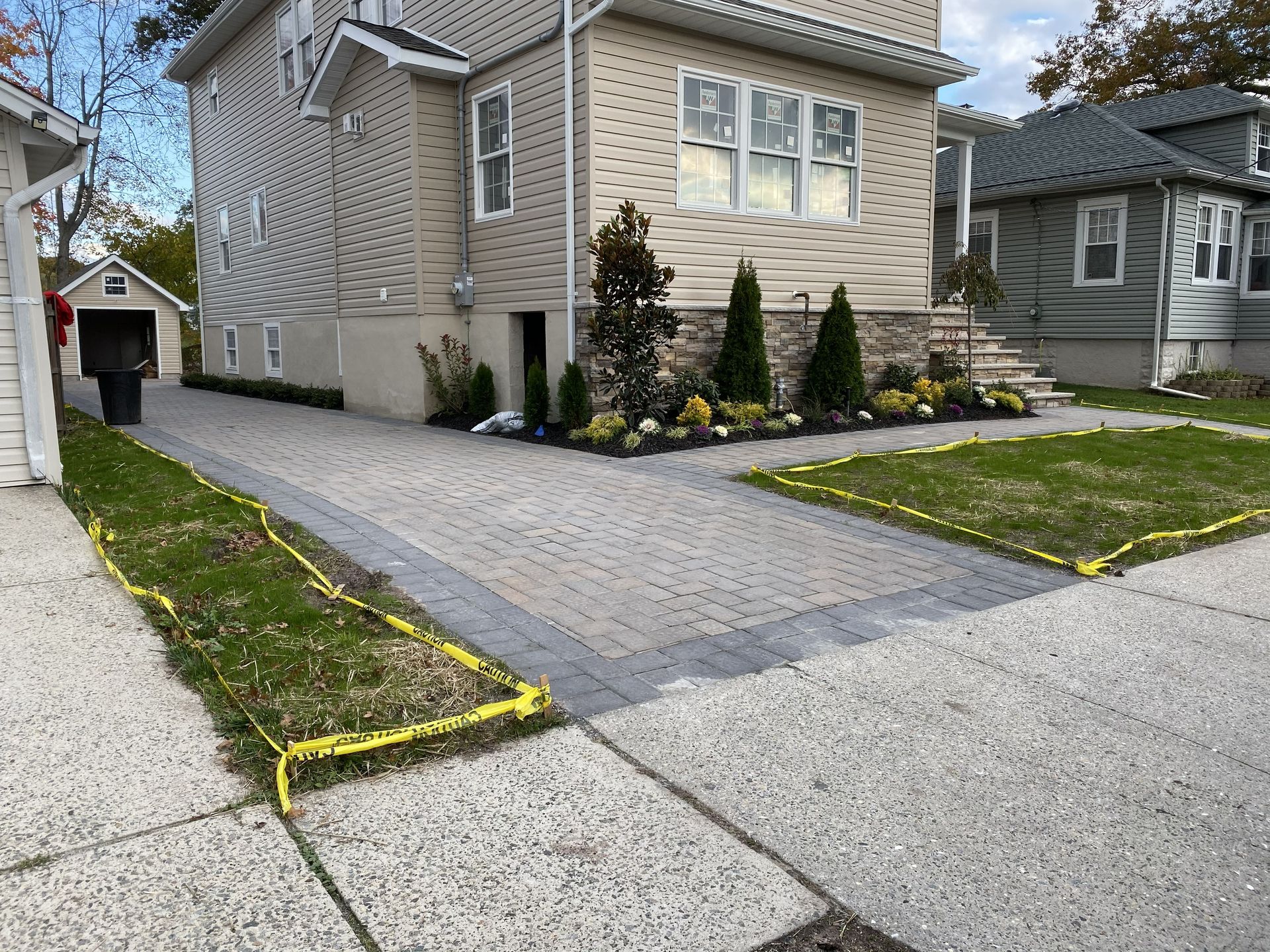 A house with a newly paved paver driveway and landscaped garden beds outlined with yellow caution tape.