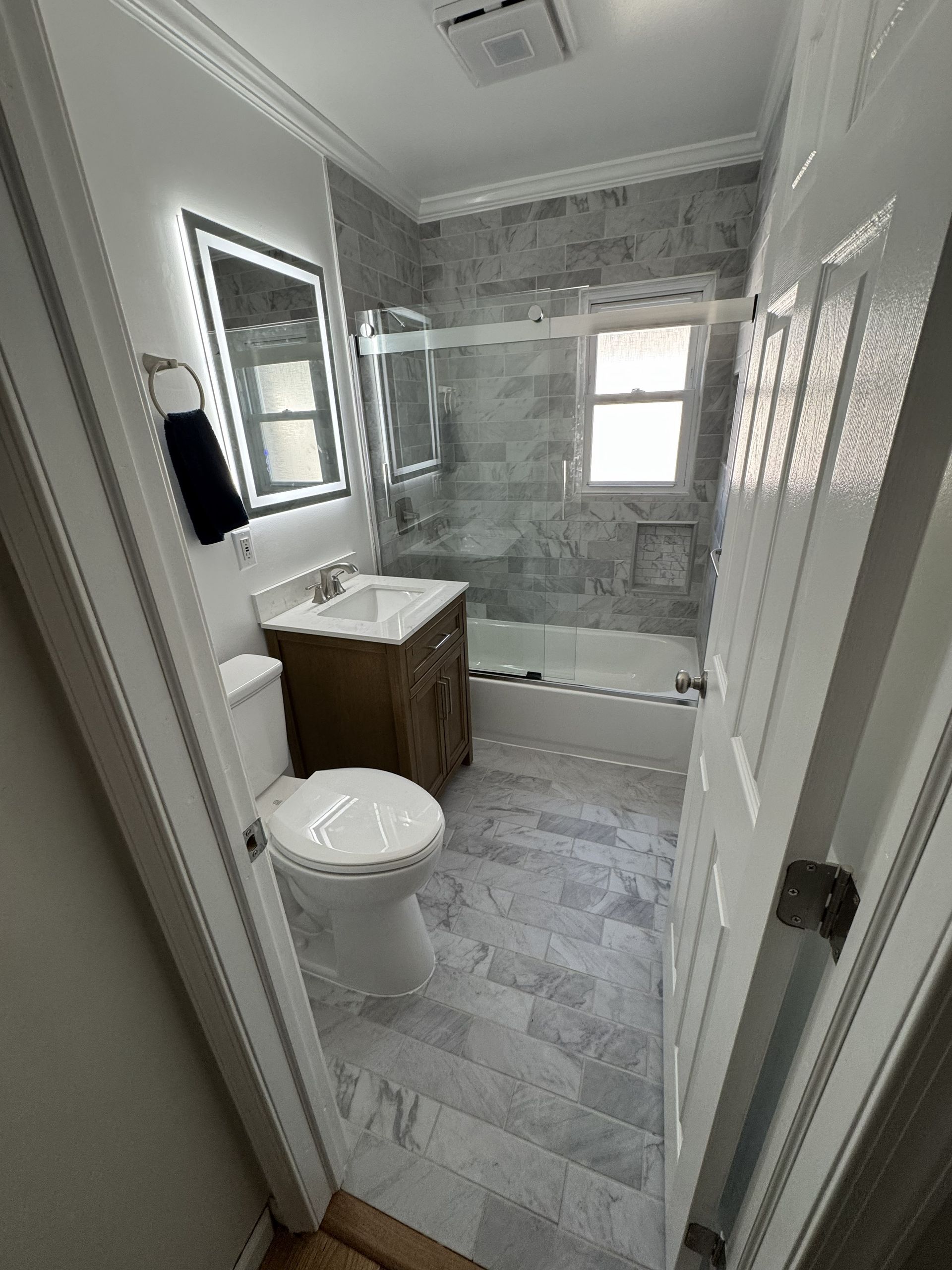 A view of a small bathroom featuring a white toilet, a wood vanity with a vessel sink, and a tiled shower-tub combo.
