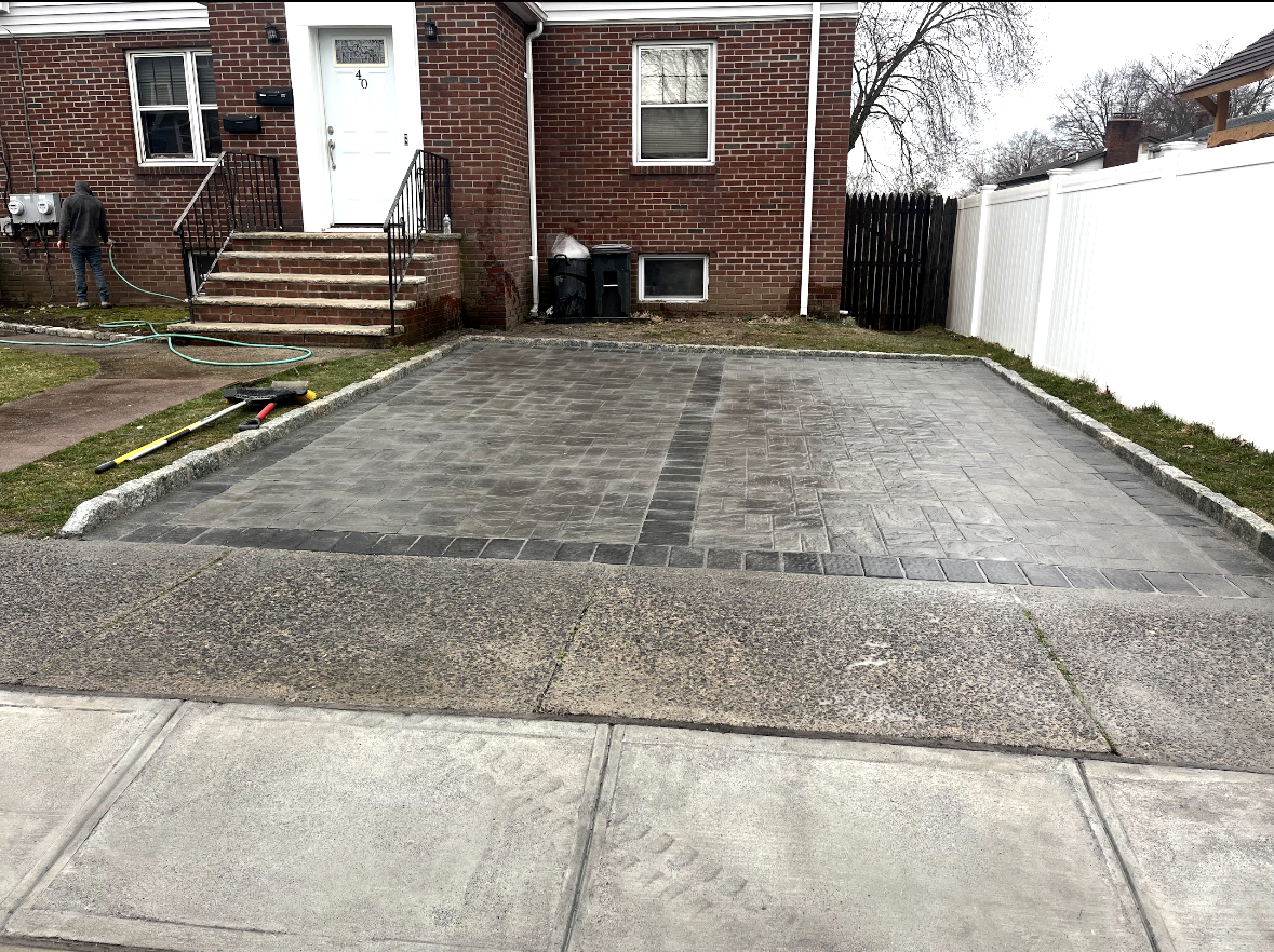 A new gray stone paver driveway sits in front of a brick house with stairs leading to a white front door.