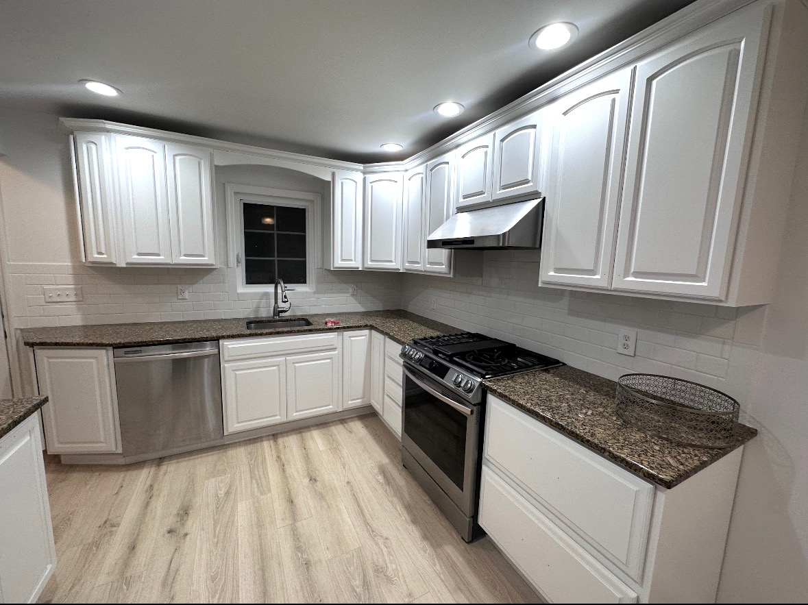 A kitchen with white cabinets, dark granite countertops, stainless steel appliances, and light wood-look floors.