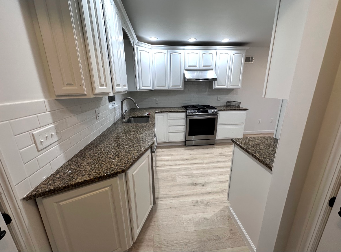 A kitchen with white cabinets, granite countertops, stainless steel stove, and light-colored wood-look flooring.