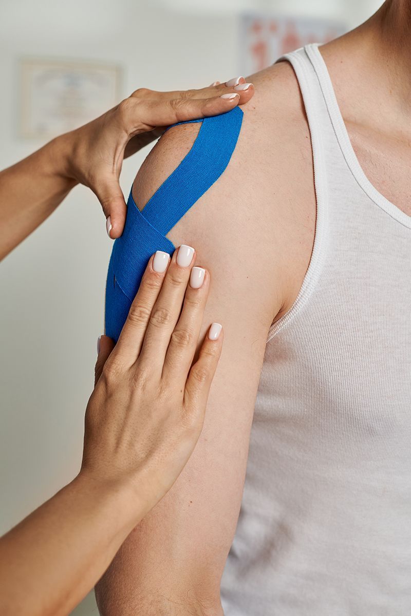 Therapist applying kinesiology tape to a patient's shoulder for support