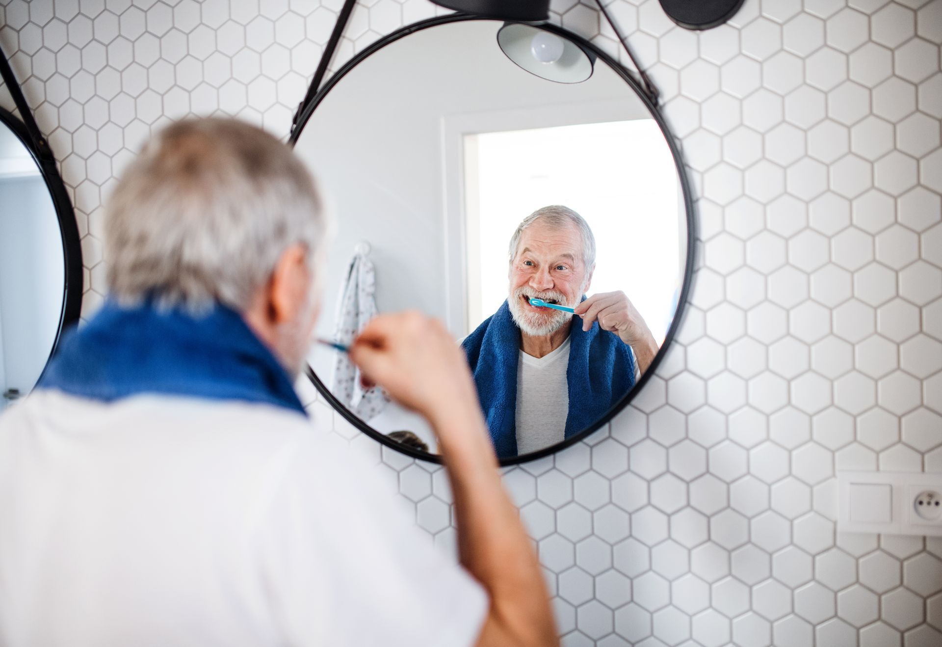 Energy conservation for bathing and grooming Senior man brushing his teeth at the bathroom mirror, an everyday grooming task occupational therapy can help make easier