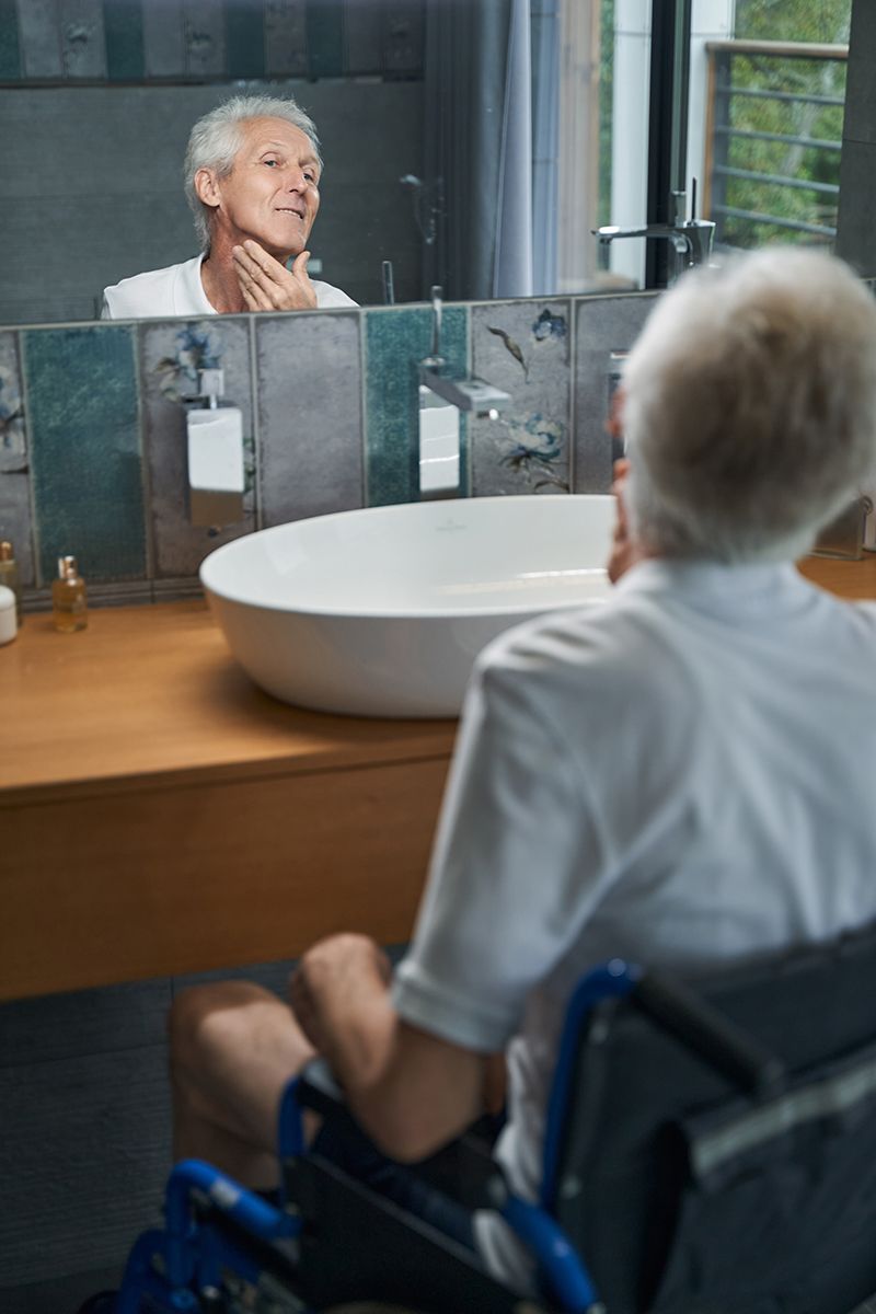 Senior man using a mobility walker while grooming independently at the bathroom sink