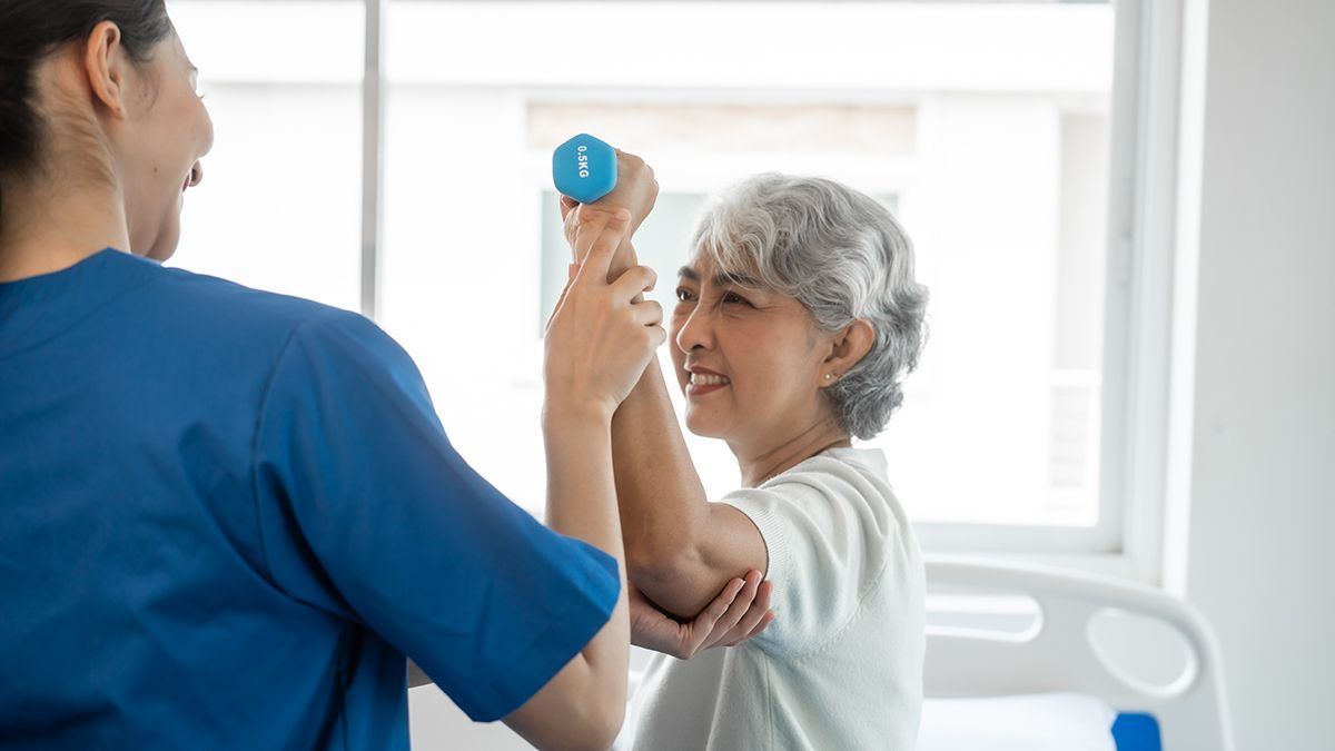 Occupational therapist guiding a senior patient through a supported arm exercise using a light weight