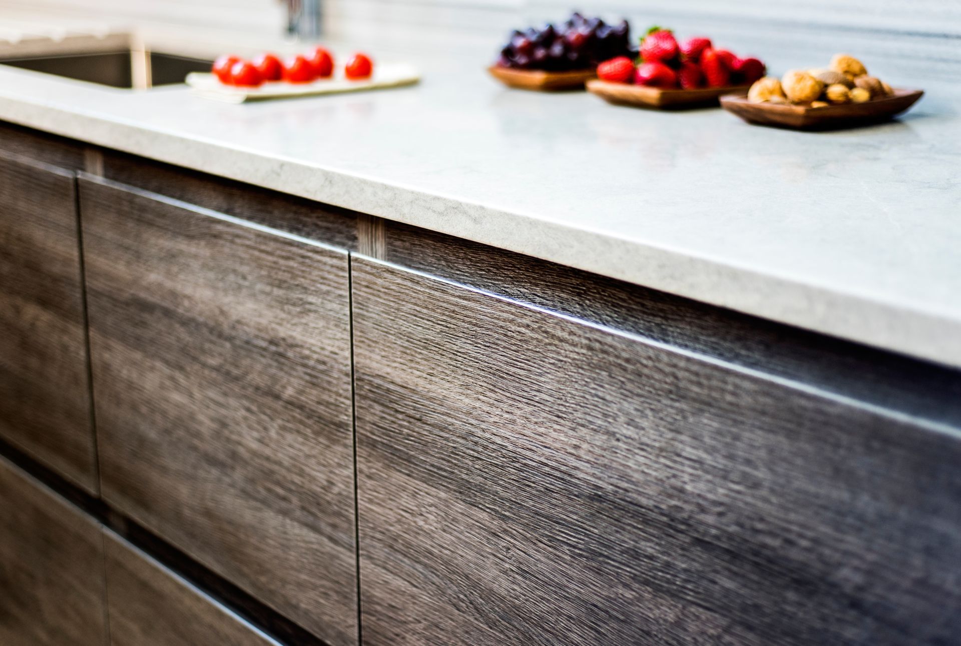 Dark wood kitchen cabinets with a light gray countertop, topped with bowls of fruit. Dark wood kitchen cabinets with a light gray countertop, topped with bowls of fruit.
