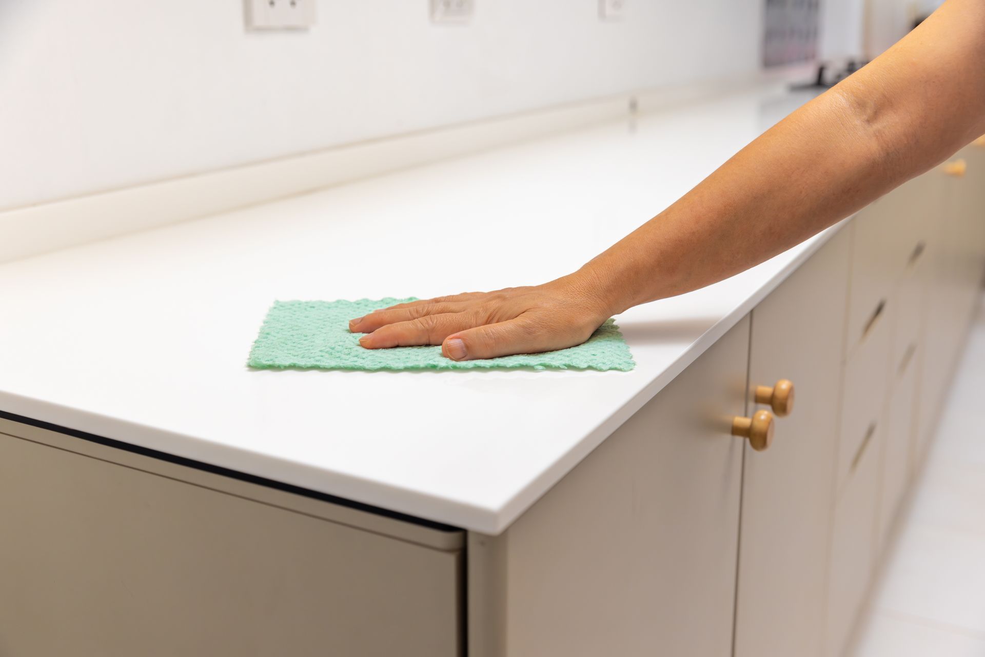 Hand wiping a white countertop with a green cloth in a kitchen. Hand wiping a white countertop with a green cloth in a kitchen.