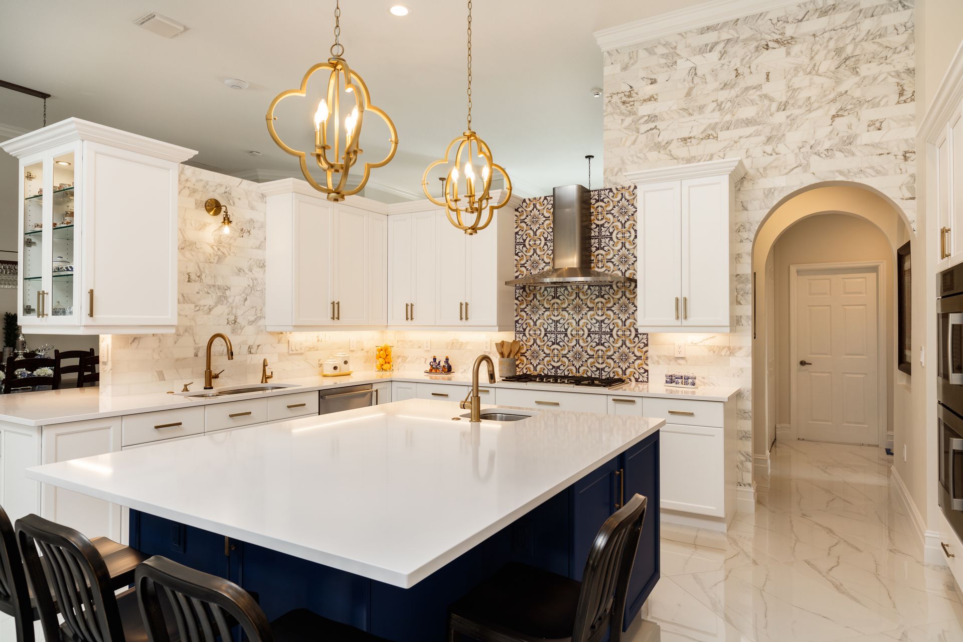 Elegant white kitchen with blue island, gold accents, marble backsplash, and hanging gold light fixtures. Elegant white kitchen with blue island, gold accents, marble backsplash, and hanging gold light fixtures.