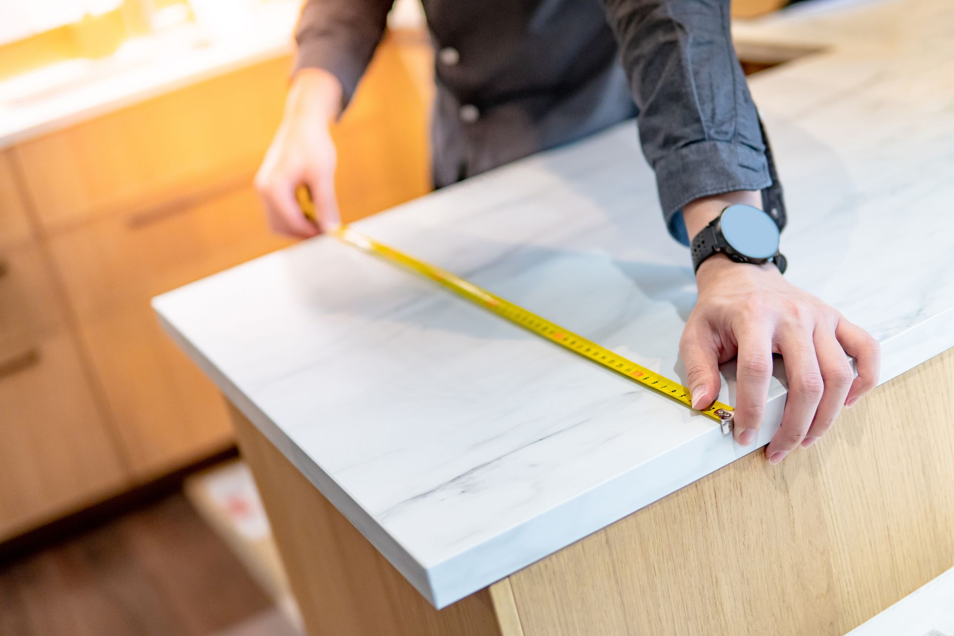 A man is using a tape measure for measuring a white granite countertop.