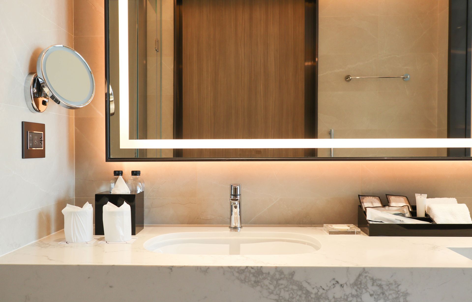 Bathroom with backlit mirror, sink, toiletries, and wall-mounted magnifying mirror. Bathroom with backlit mirror, sink, toiletries, and wall-mounted magnifying mirror.