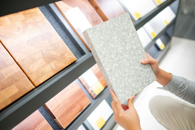 Gray speckled countertop sample held in front of wood-patterned showroom display.
