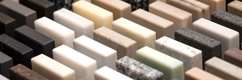 Wooden kitchen with cabinets, countertops, and appliances. Close-up of a variety of stone countertop samples in various colors and patterns.
