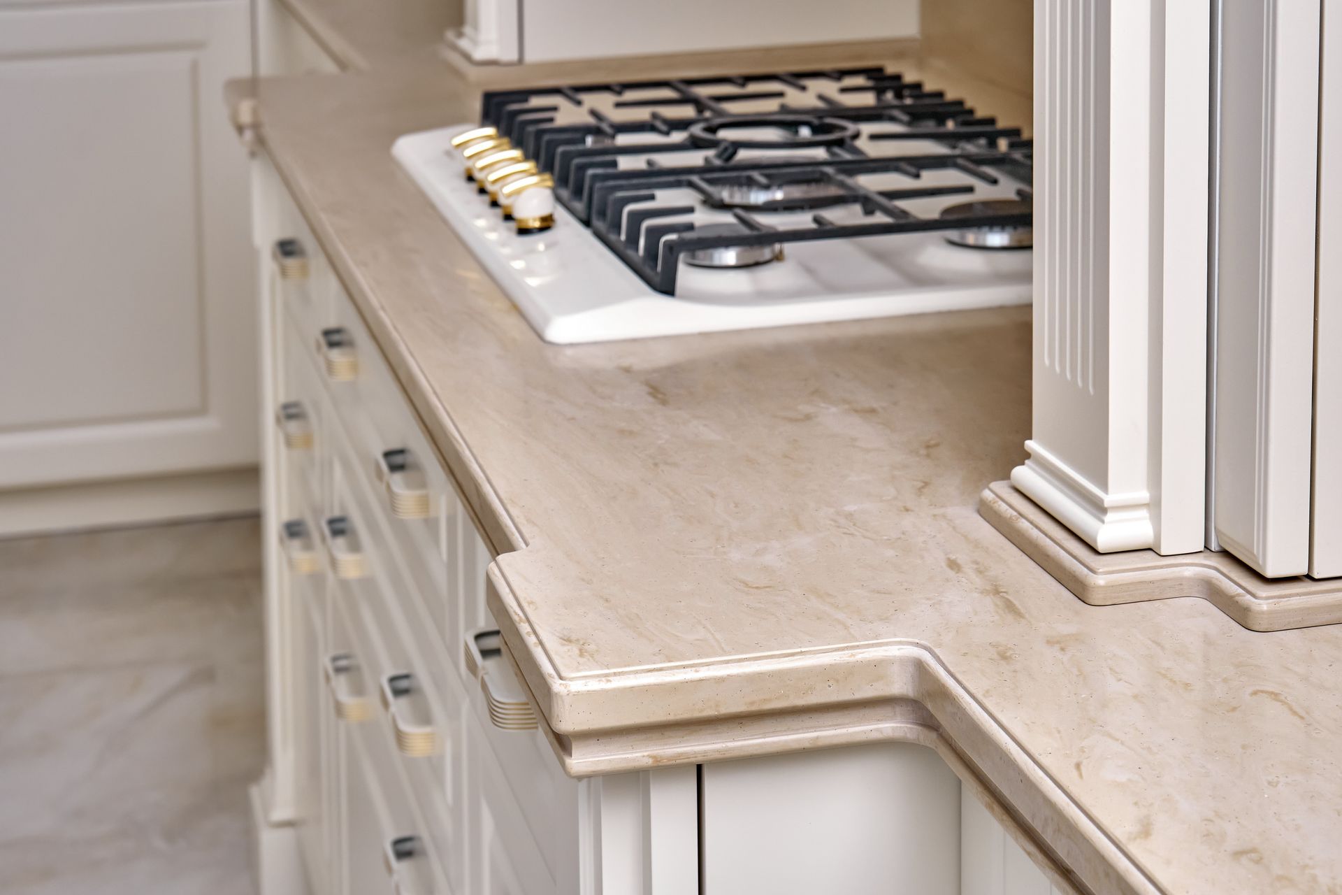 Beige marble countertop with a built-in gas stove and white cabinets in a kitchen. Beige marble countertop with a built-in gas stove and white cabinets in a kitchen.