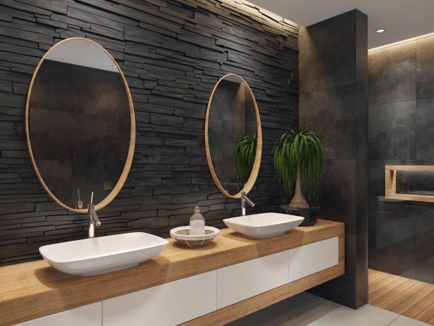 Modern bathroom vanity with double vessel sinks, wood countertop, round mirrors and dark stone wall.