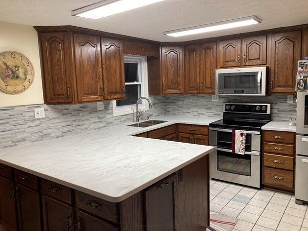 Kitchen with dark wood cabinets, light countertops, stainless steel appliances, and white and gray backsplash.
