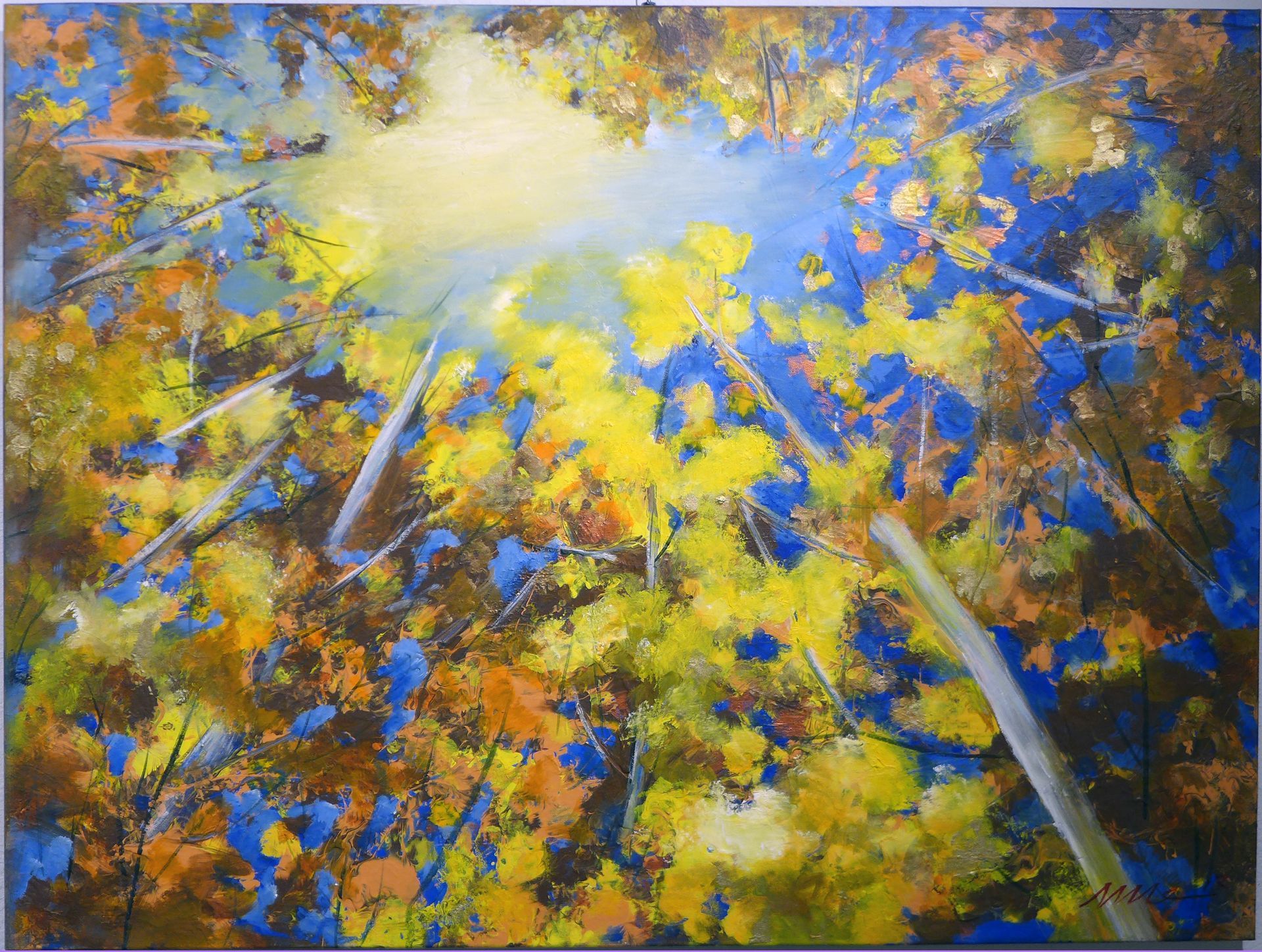 Sunlit autumn trees with yellow and blue leaves seen from below against a bright sky