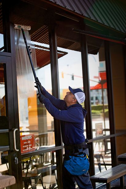 Window cleaner using a black squeegee on a glass storefront window with reflections of the sky and building.