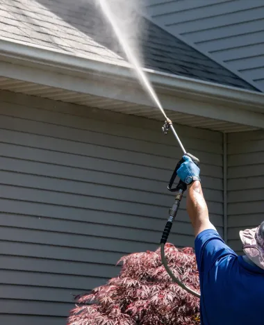 Person pressure-washing a house roof with a long spray wand