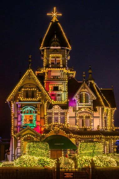 Illuminated Victorian-style house at night, covered in colorful holiday lights and topped with a glowing star