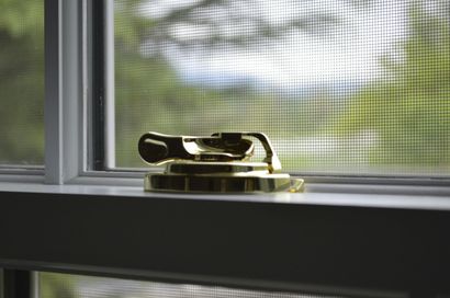 Brass doorstop on a windowsill beside a screened window with blurred greenery outside