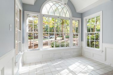 Bright sunroom with large arched windows, white trim, and tiled floor overlooking a garden.