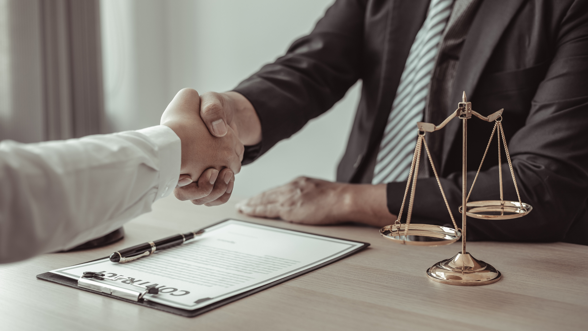 Handshake between two people at a desk with legal documents and scales of justice.
