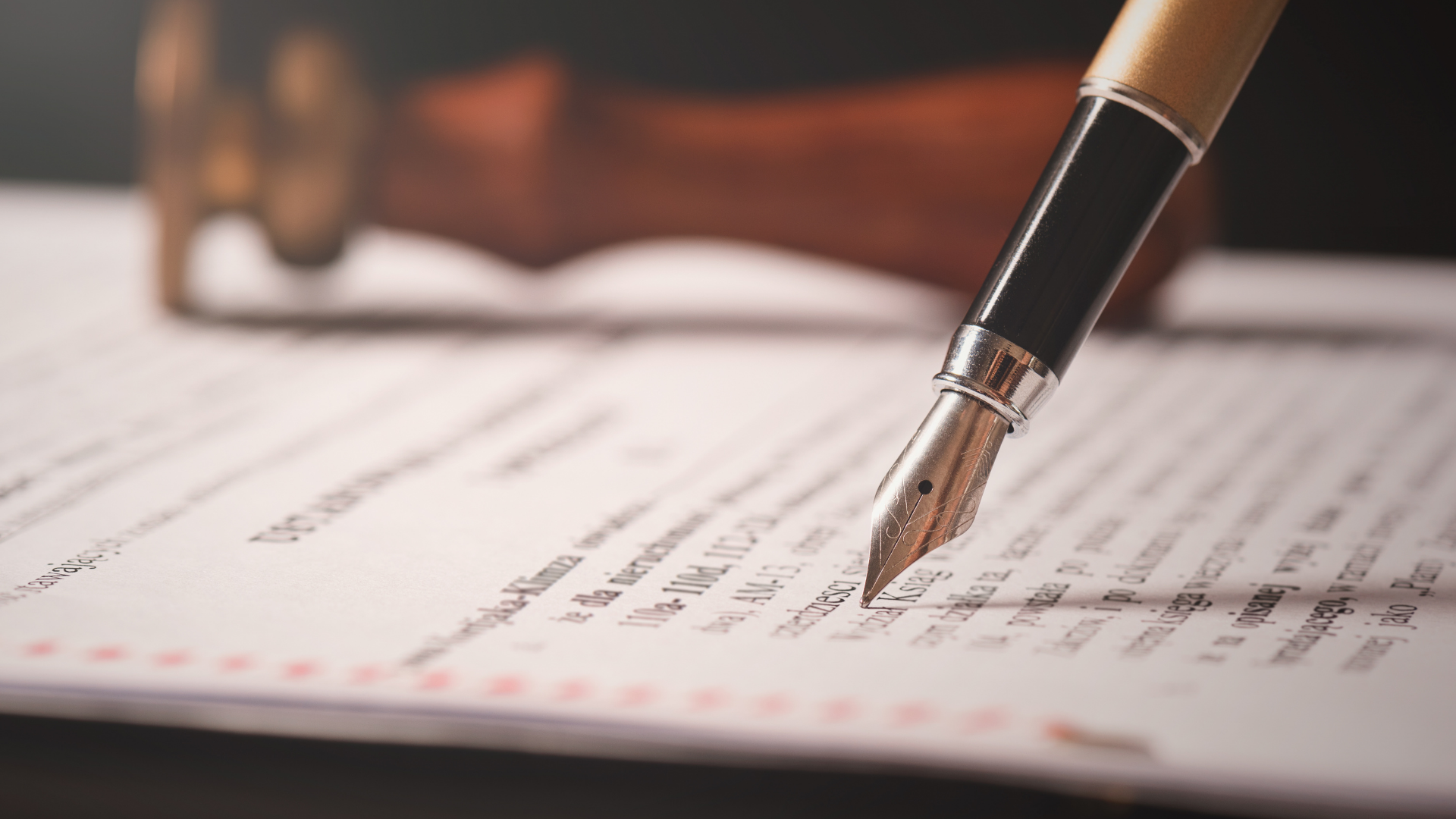 Pen poised over a form on a desk, with a blurred hand in the background.