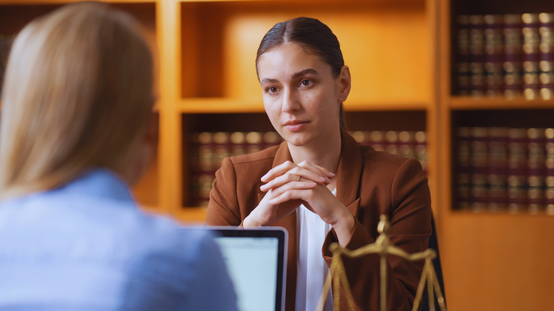 Attorney listening across a desk in a law office, with bookshelves and a scales of justice statue in the background