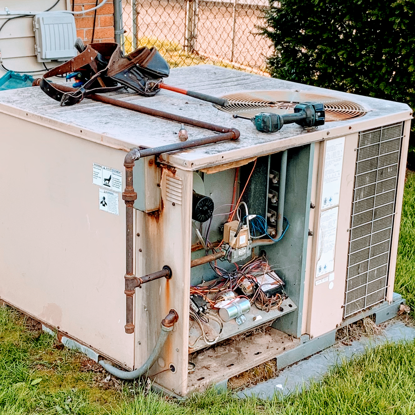 Outdoor air conditioning unit with open side, tools on top, rusty pipes.