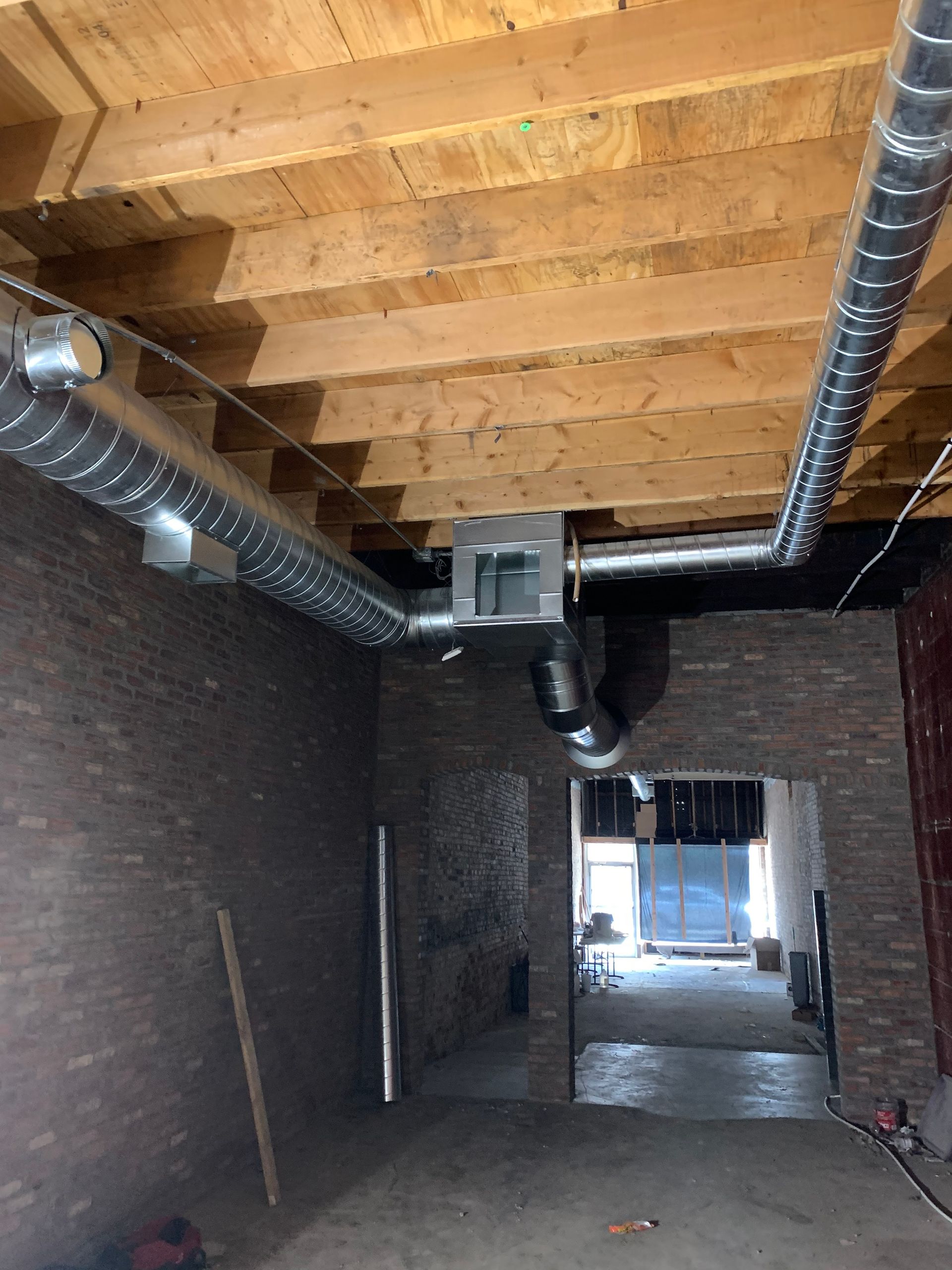 Interior view of a room under construction with exposed wood beams, brick walls, and HVAC ductwork.