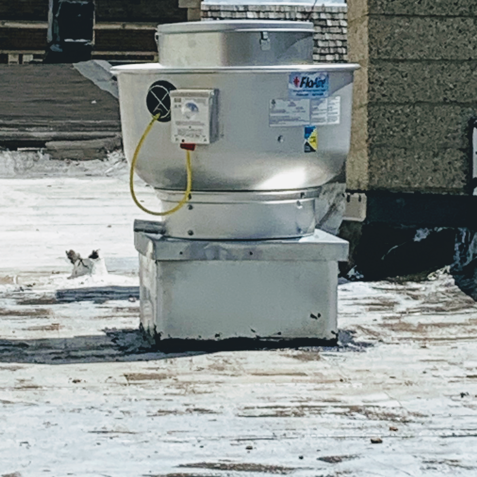 Silver rooftop exhaust fan on a weathered, snowy rooftop.