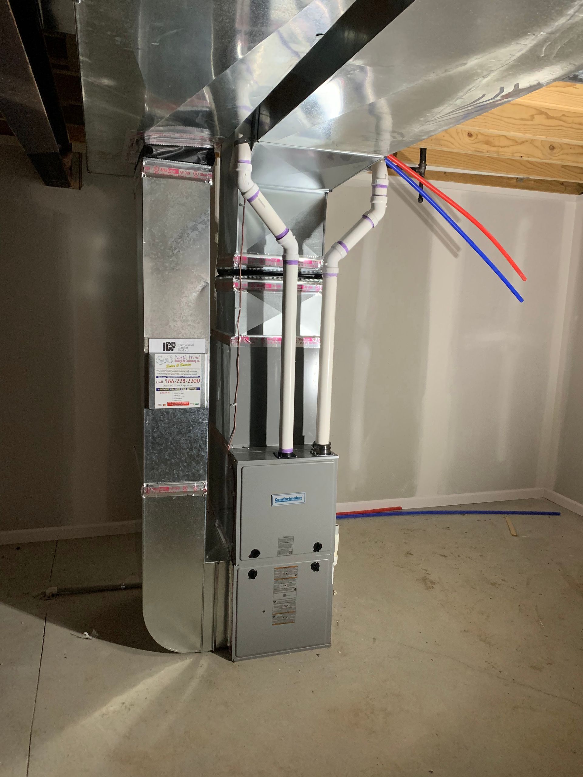 Furnace and ductwork in a basement setting. Metal ducting and pipes against a gray wall and floor.